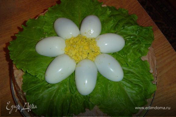 А теперь украшаем готовый торт.На торт кладем листья салата, отварные яйца разрезаем вдоль на две части, удаляем желток, а белки выкладываем виде цветка. Желток растираем и выкладываем в центр «цветка».