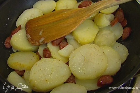 Разогреть в сковороде, которую можно ставить в духовку, растительное масло, обжарить картофель и колбаски до золотистого цвета, затем снять с огня.