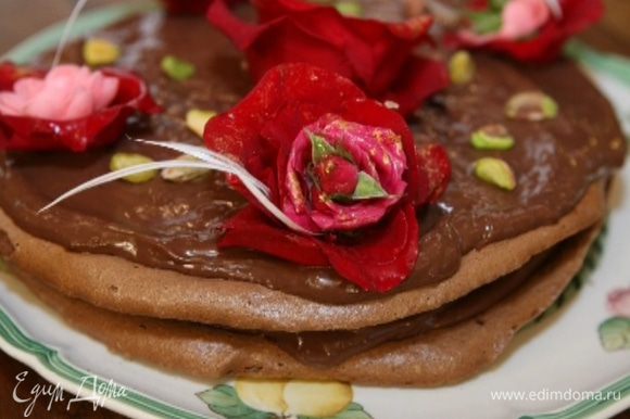 Смазать остывшие меренги шоколадным кремом, уложить одну на другую и украсить сверху, например, живыми красными розами, и присыпать фисташками.
