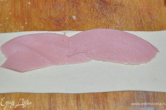 Колбасу разрезать на полоски и положить полосочку колбаски на тесто.