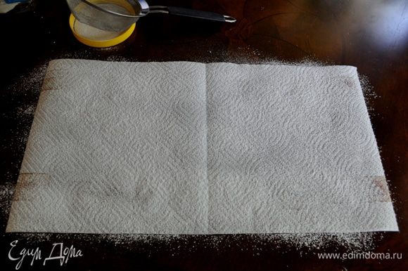 Подготовим бумажное полотенце или кухонное чистое, постелив его на стол под размер противня с бисквитом.Посыпем сах.пудру ситечком на полотенце.