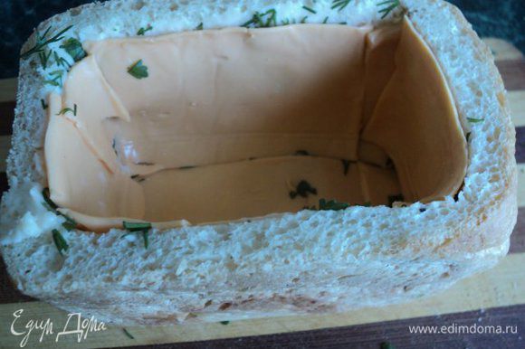 Смазать стенки и дно хлеба внутри тонким слоем мягкого плавленого сыра, посыпать зеленью и выложить пластинками сыра.