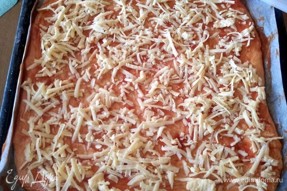 Затем раскатываем тесто, из этого количества продуктов у меня получили две большие пиццы. Основу для пиццы смазываем томатным соусом и посыпаем тертым сыром.