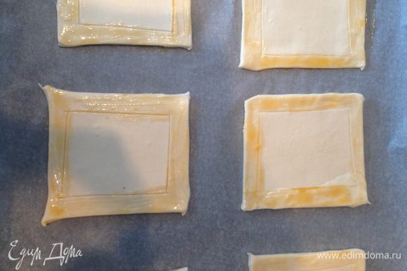 Тесто разрезать небольшие квадратики. Надрезать (не протыкая тесто насквозь) тесто отступая по 2 см с краев. Смазать края желтком.