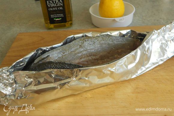 При помощи 2 слоёв фольги зафиксируйте рыбу в вертикальном положении, оставив верхний разрез открытым. Не забудьте предварительно хорошо смазать оливковым маслом внутреннюю сторону фольги и особенно рыбий хвост. Иначе он высохнет.