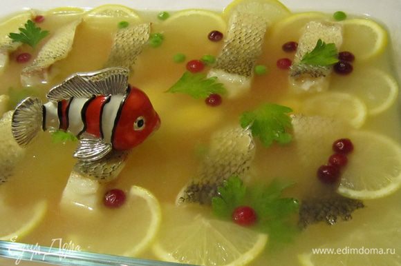 Когда рыбный бульон немного застынет, выложите на него кусочки рыбы (оставляя промежутки между кусочками), половинки перепелиных яиц, цветочки из моркови, дольки лимона, листики петрушки, клюкву и зеленый горошек. Залейте бульоном так, чтобы его слой над куском рыбы был 0,5–0,8 см и снова поставьте в холодное место для застывания.