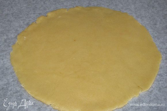 Достать тесто из холодильника, разделить на две неравные части. Большую часть раскатать в круг и перенести на противень, застеленный пекарской бумагой.