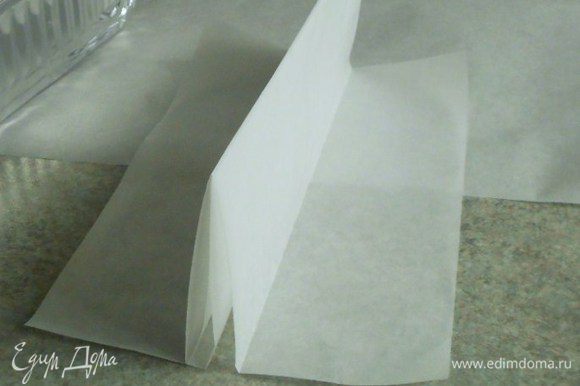 Возьмите лист пекарской бумаги 30 х 20 см и сложите его так, чтобы в центре образовалась складка из слоёв бумаги высотой 8 см. Это приспособление поможет разделить форму для выпечки пополам и одновременно выпекать 2 разноцветных коржа.