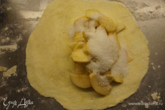 Достать тесто из холодильника, разделить на 5 - 6 частей. Каждую часть раскатать в блинчик, не очень тонко. А затем по принципу лепки вареников, на одну половину блина положить начинку из яблок и посыпать сахарным песком - 1-2 десертных ложки в каждый пирог.