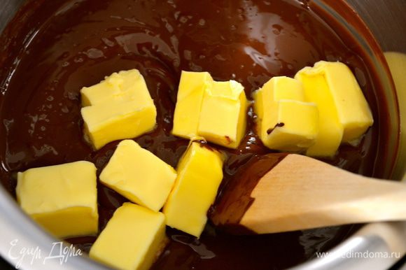 Тем временем, шоколад поломать на кусочки и поставить плавиться на водяной бане. Как только шоколад растает, добавить 100 г сливочного масла кусочками и как следует размешать. Отставить в сторону остывать.