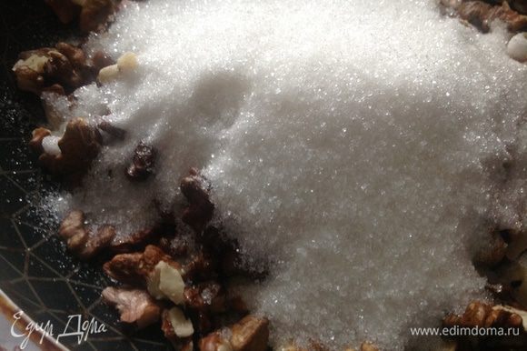 Через пару минут к орехам добавить сахар и жарить, непрерывно помешивая лопаткой.