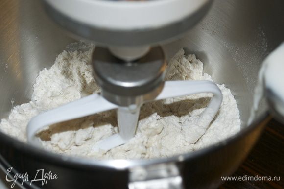 Включить тестомешалку на медленную скорость и начать перемешивать все сухие ингредиенты, постепенно вливая теплое молоко.