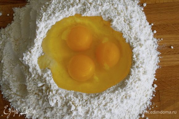 На поверхность стола (или специальной доски для теста) выложить горкой всю муку. Сделать рукой в центре углубление, наподобие лунки. Добавить щепотку соли и разбить в лунку яйца.