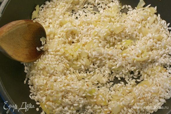 Следите, чтобы лук не зажарился! Как только лук посветлеет, всыпать рис. Перемешать и дать обжариться вместе с луком 1-2 минуты, помешивая.