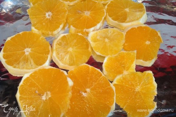 Очистите апельсины, нарежьте кружочками, выложите на противень застеленный фольгой.