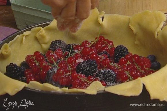 Выложить на тесто ягоды, немного присыпать их сахаром и загнуть края теста, накрыв им ягоды — середина должна остаться открытой.