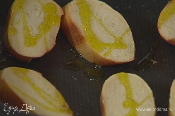 Багет нарезать, выложить на противень, сбрызнуть оливковым маслом и отправить в духовку под гриль на 2–3 минуты.