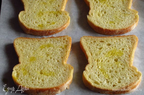 Ломтики хлеба сбрызнуть оливковым маслом, выложить на противень с пергаментом и запечь в разогретой до 180 С духовке 6 минут.