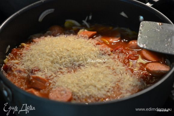 Добавить в блюдо колбасу, томаты баночные порезанные кубиками 400 г, бульон или воду, рис. Довести до кипения, убавить огонь и закрыть крышкой. Готовить до готовности риса примерно 25 минут. Помешиваем.