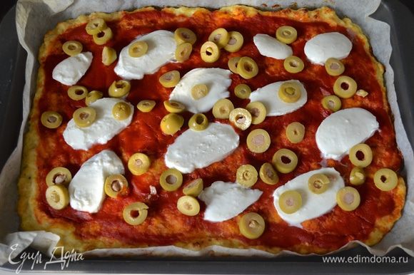 Через 15 минут достать противень и выложить на "пиццу" нарезанные предварительно сыр моцарелла и зеленые оливки.