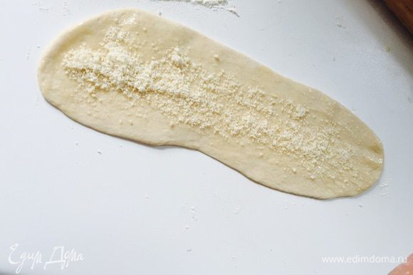 Раскатываем в тонкий узкий пласт толщиной 3-4 мм. Смазываем растопленным сливочным маслом, посыпаем пармезаном.