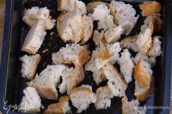 Приготовить крутоны: хлеб поломать руками на неровные кусочки и выложить в небольшой глубокий противень.