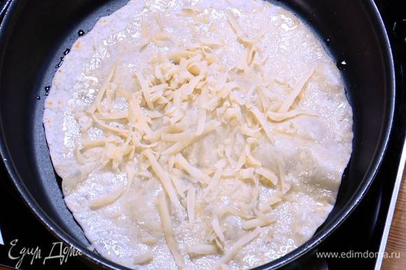 Разогреть в отдельной сковороде оставшееся оливковое масло и прогреть тортилью, затем перевернуть и посыпать натертым сыром. Когда сыр слегка расплавится, перевернуть лепешку еще раз, снова посыпать сыром и переложить на тарелку. Так же прогреть вторую тортилью.