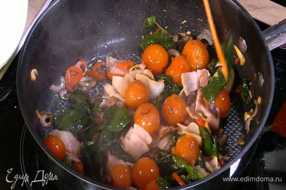 Бекон нарезать небольшими кусочками, добавить в сковороду с помидорами и шпинатом, перемешать и обжарить.