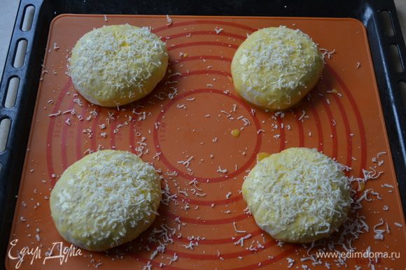 Выложить их на противень, застеленный пекарской бумагой, (или на силиконовый коврик). Смазать булочки яйцом и обильно посыпать натертым на мелкой терке пармезаном.