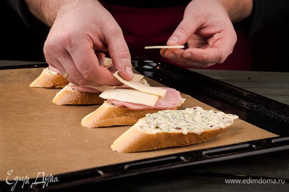 На каждый кусочек багета выложить топпинг, сверху накрыть его ветчиной и слайсом сыра. Поставить в духовку на 5 минут при 180°С.