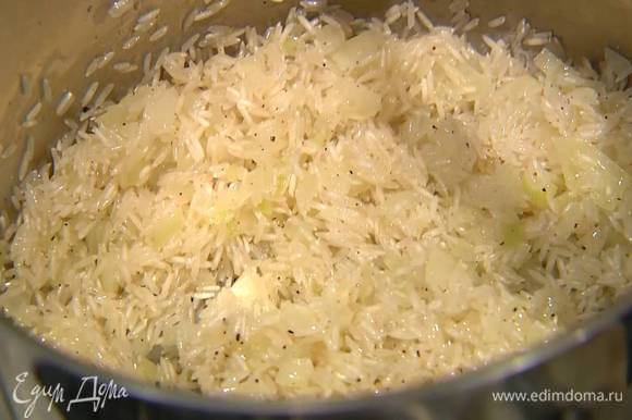 Всыпать к луку рис, перемешать и обжаривать около минуты, затем залить горячей водой и варить рис до готовности.