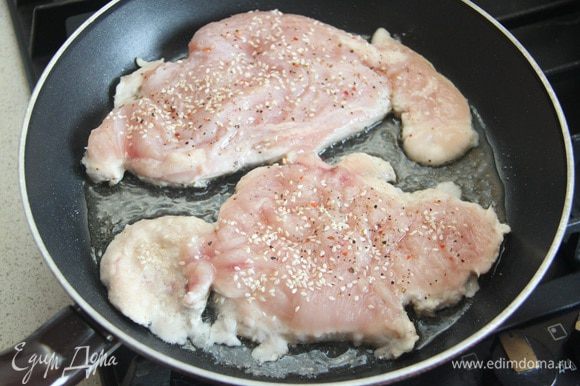На раскаленную сковороду налить растительное масло, выложить куриные отбивные перченой стороной вниз. Теперь посолить, поперчить и посыпать кунжутом верхнюю сторону. Жарить на сильном огне ровно 3,5 минуты.