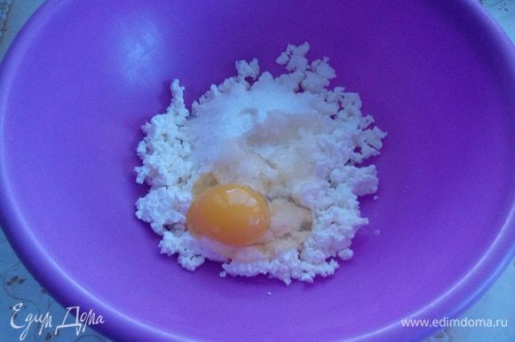 В чашку выкладываем творог «Домик в деревне». Хорошо разминаем вилкой. Добавляем щепотку соли, сахар и взбитое яйцо. Хорошо перемешиваем.