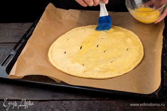 Накройте начинку вторым пластом теста. Защипните края пирога и смажьте его сверху взбитым яйцом.
