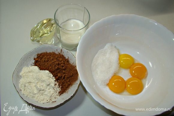 Приготовить темный бисквит. Для этого смешать венчиком в миске желтки, сахар, муку с какао, влить теплое молоко, растительное масло.