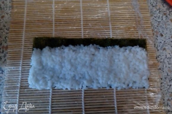 На шершавую поверхность нори выложить рис, оставит ~1 см листа не покрытым.