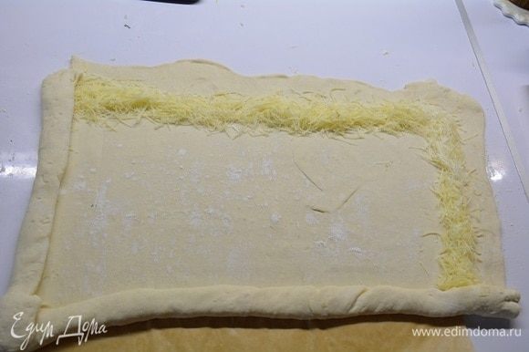 Растелить лист пекарской бумаги. На нем раскатать тесто в прямоугольный пласт. По краям насыпать тертый сыр пармезан, отступив от края чуть-чуть.