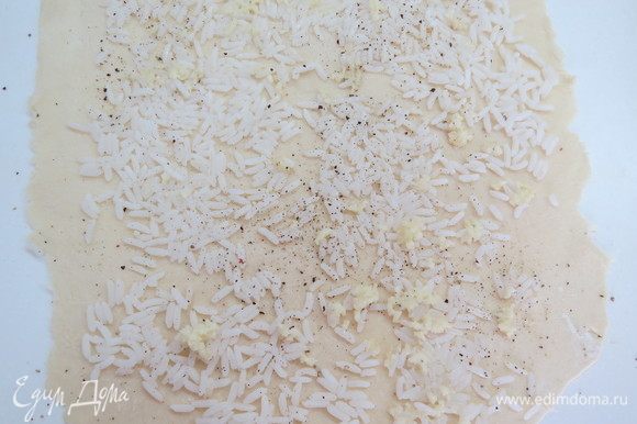 Через чеснокодавку выдавливаем чеснок и распределяем равномерно поверх риса. Прокатываем аккуратно скалкой, чтобы рис вдавился в тесто.