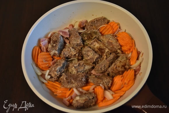 К бекону выложить крупнонарезанную морковь и лук. Обжарить в течение 5 минут и добавить мясо.