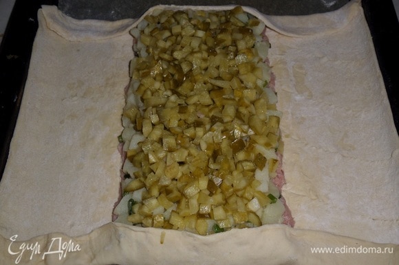 Поверх картофеля выкладываем нарезанные маринованные огурцы, равномерно распределяем. Подгибаем края пласта теста сверху и снизу.