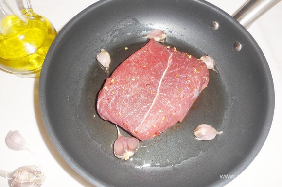 На сковороду налить оливковое масло, добавить раздавленные зубчики чеснока. Разогреть масло и выложить мясо.