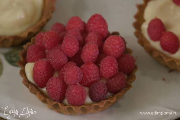 Наполнить тарталетки охлажденным кремом и украсить ягодами малины.