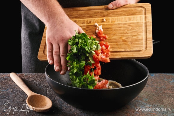 Добавьте в сковороду помидоры, зелень, перемешайте и обжаривайте до готовности кальмаров.