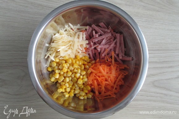 Из банки с консервированной кукурузой слейте жидкость. Сырую морковь натрите крупно, так же натрите полутвердый сыр. Колбасу нарежьте соломкой.