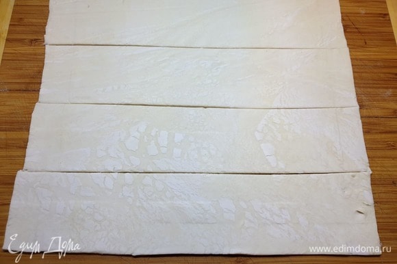 Размороженное слоеное тесто немного раскатываем и нарезаем полосками, шириной 6 см.