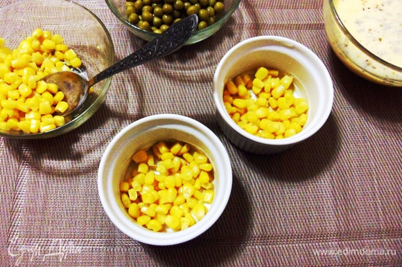Смазать керамические формочки небольшим количеством оливкового масла и выложить по столовой ложке консервированной кукурузы в каждую.