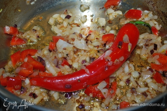 К луку добавьте красный болгарский перец, нарезанный кубиками, и целый острый перчик. Обжарьте все вместе в течение 3–4 минут.