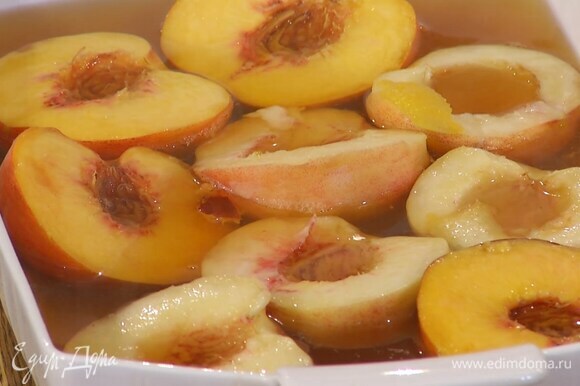 Персики разрезать пополам и, удалив косточки, выложить в жаропрочную форму срезами вверх, а затем залить горячим сиропом.