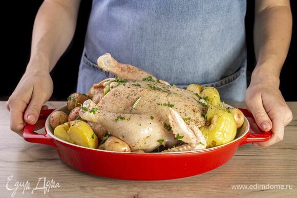 Переложите курицу на противень. Добавьте картошку, моченые яблоки и розмарин. Запекайте в духовке 1 час при 180°C. Каждые 20 минут поливайте маслом.