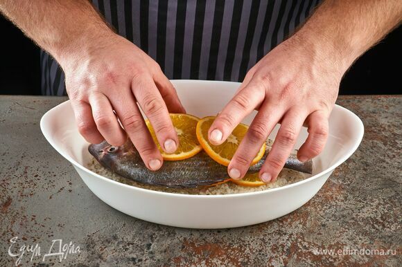 На соль уложите рыбу целиком, сверху — дольки апельсина.